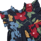 Close-up of a children's dress with a dark navy floral print, featuring red, blue, and mustard yellow flowers with green leaves and ruffled sleeves.