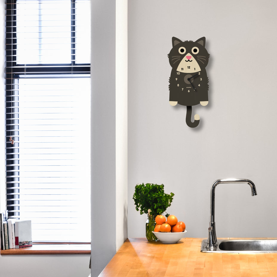 Cat-shaped wall clock on a kitchen wall with a window and countertop in the background.