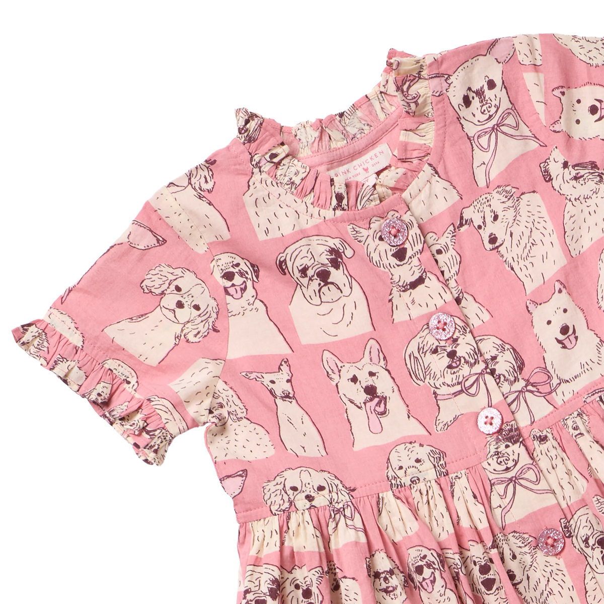 Pink short-sleeve dress with a dog print pattern, featuring ruffled trim at the neckline and a buttoned front, shown on a white background.