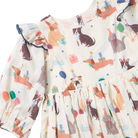 A close-up of a baby dress with a cream-colored base and an all-over print of dachshunds, birthday candles, party hats, balloons, and gift boxes. The dress features ruffled long sleeves with dark blue trim and a ruffled bodice and skirt.