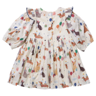 A baby girl's long-sleeve dress with a cream-colored base and an all-over print of dachshunds, balloons, and birthday candles. The dress features ruffled shoulders and a gathered skirt