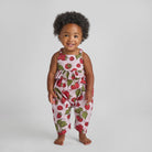 Child wearing a strawberry print romper on a plain background