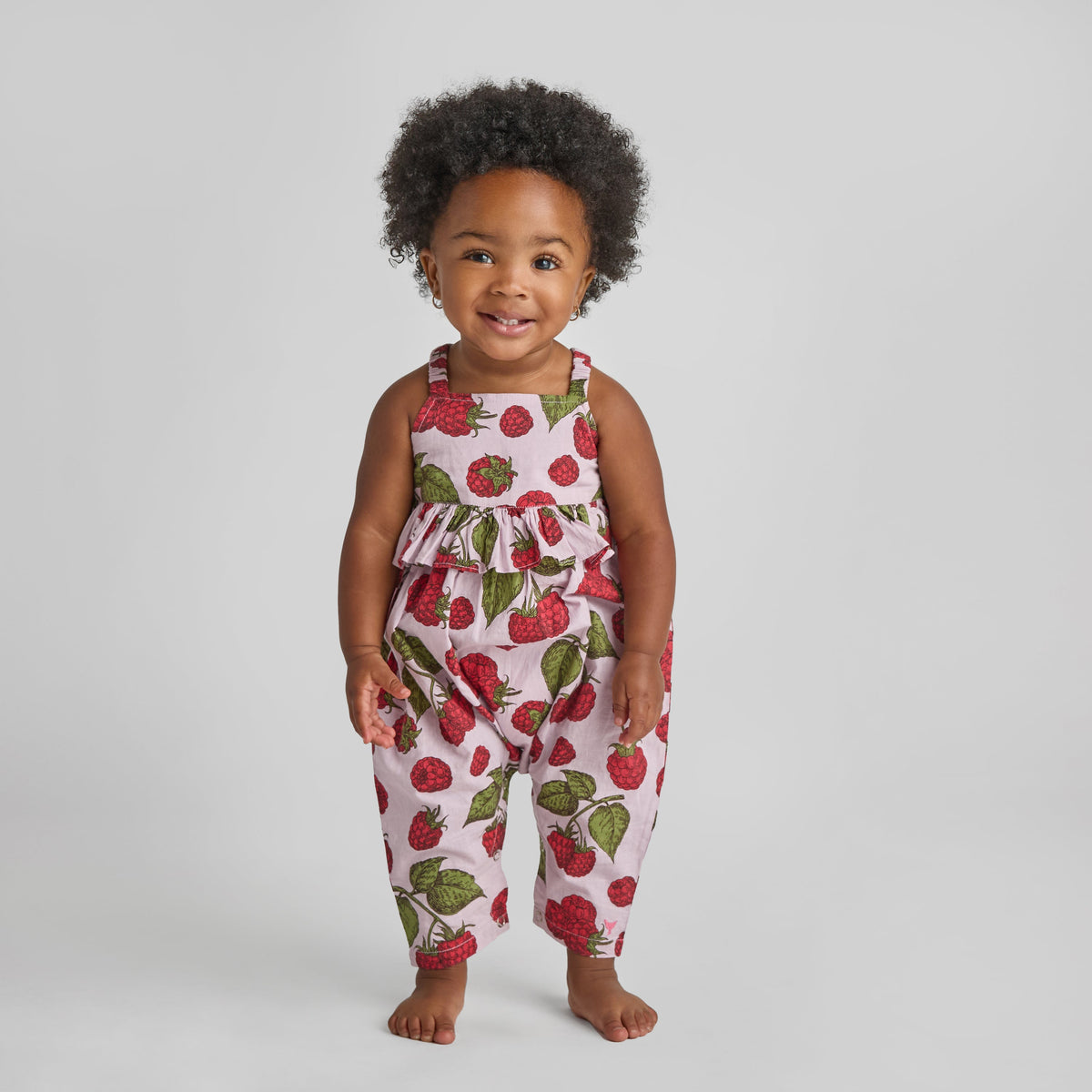 Child wearing a strawberry print romper on a plain background