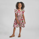 Young girl wearing a dress with a strawberry pattern on a plain background