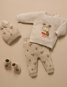 Baby outfit set with sweater, pants, hat, and shoes on a beige background