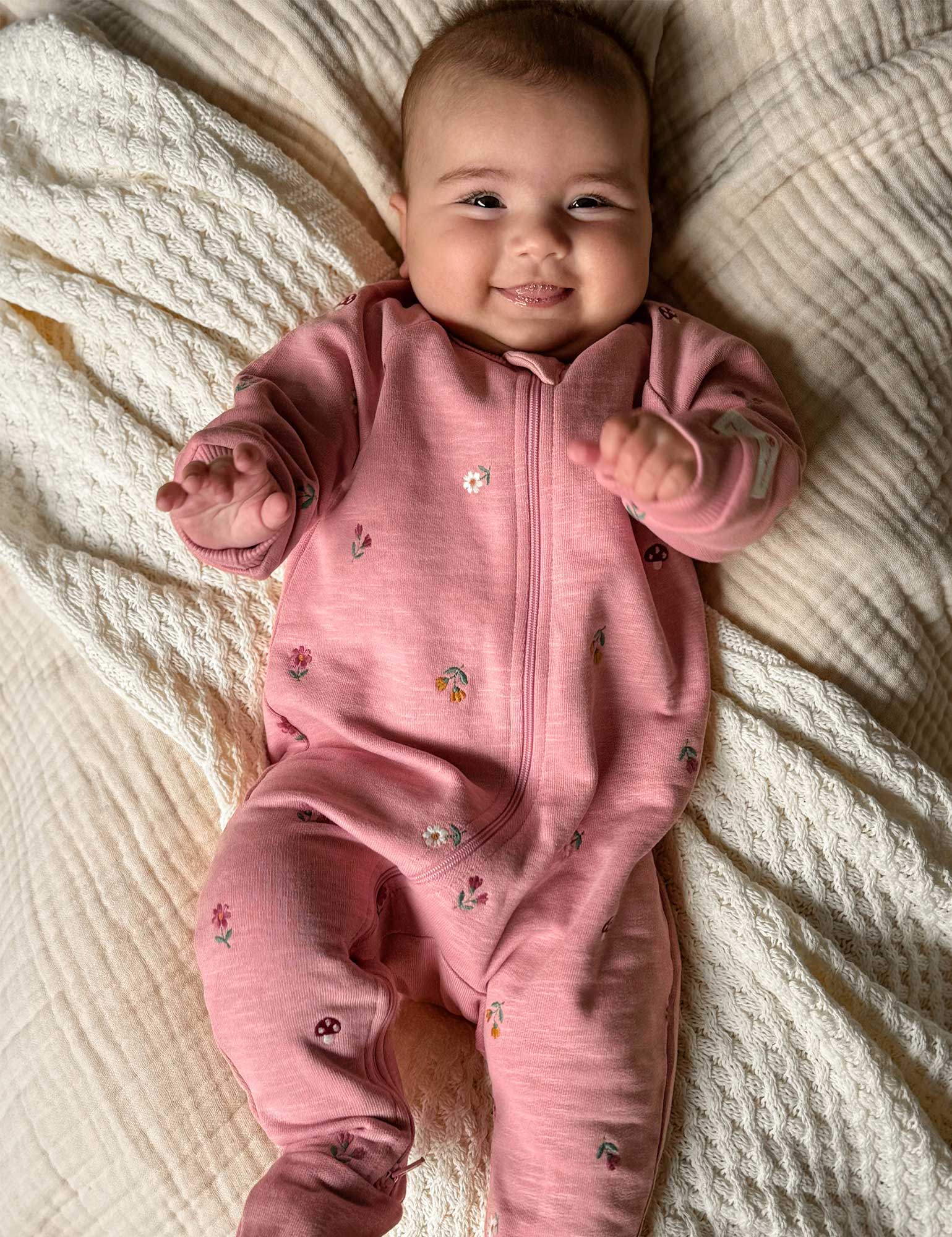 Baby in a pink onesie lying on a textured blanket