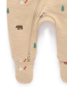 Close-up of a baby footed sleeper in a warm beige heathered fabric, featuring a small woodland animal print including a bear, owl, fox, and pine tree, with a zippered leg.