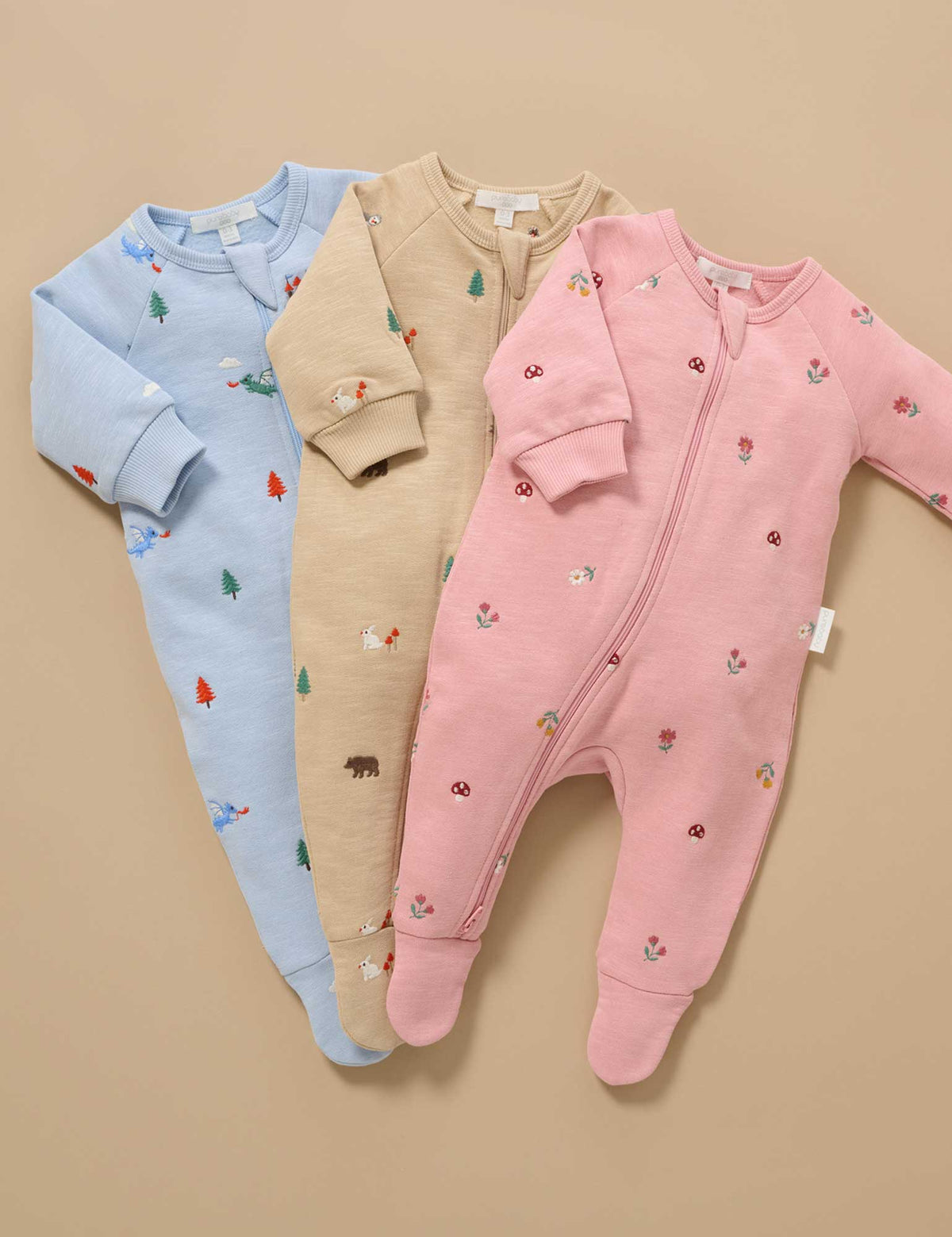 Three baby onesies in blue, beige, and pink with animal prints on a beige background