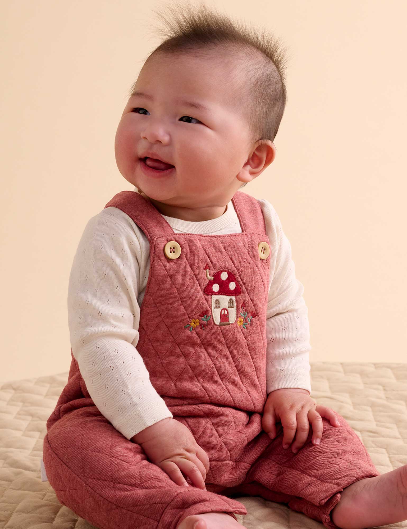 Baby wearing a pink quilted romper with a mushroom design on a beige background