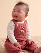Baby wearing a pink quilted romper with a mushroom design on a beige background