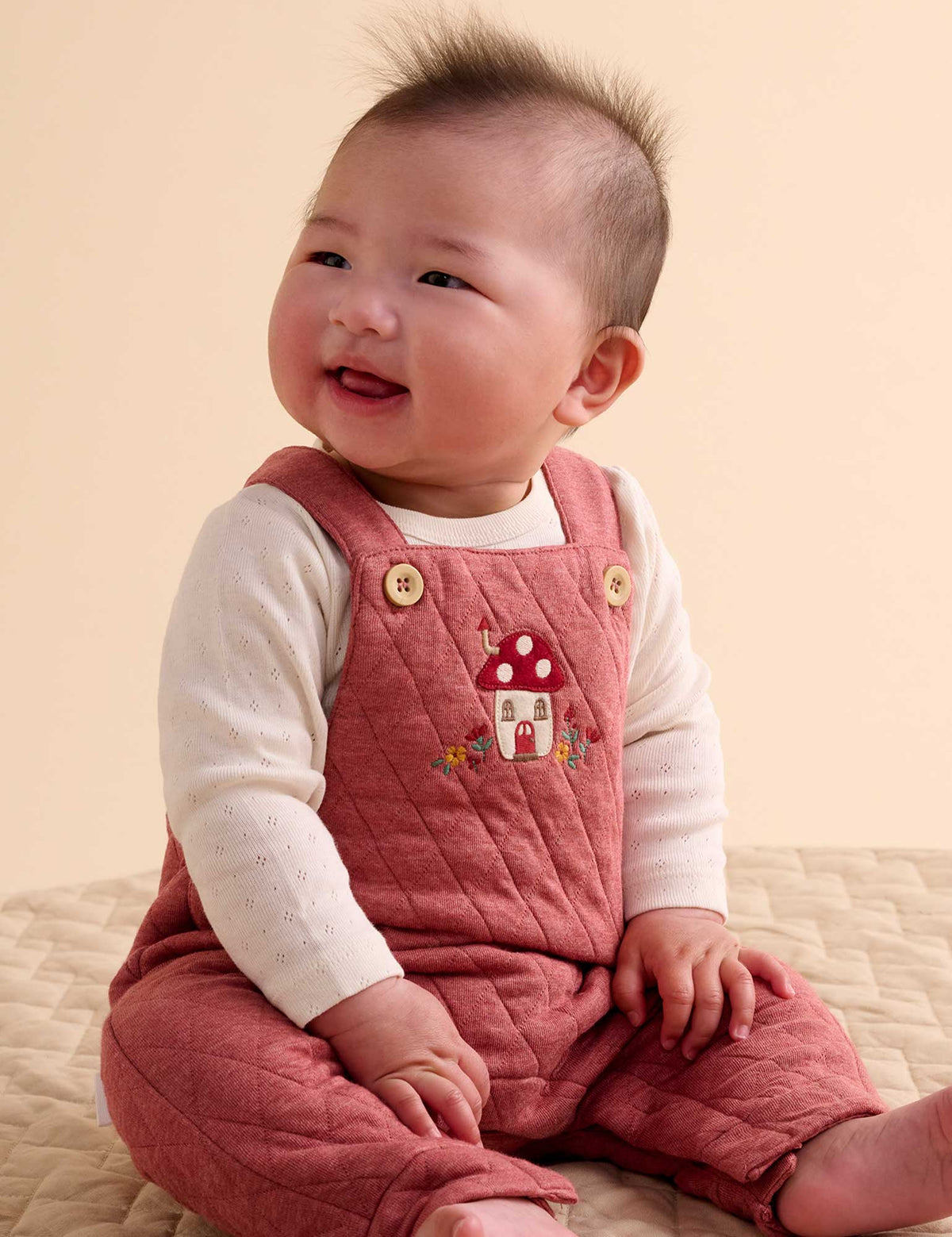 Baby wearing a pink quilted romper with a mushroom design on a beige background