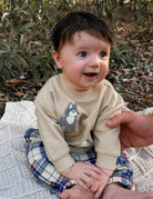 Baby wearing a beige sweater with a fox design, sitting outdoors on a blanket.