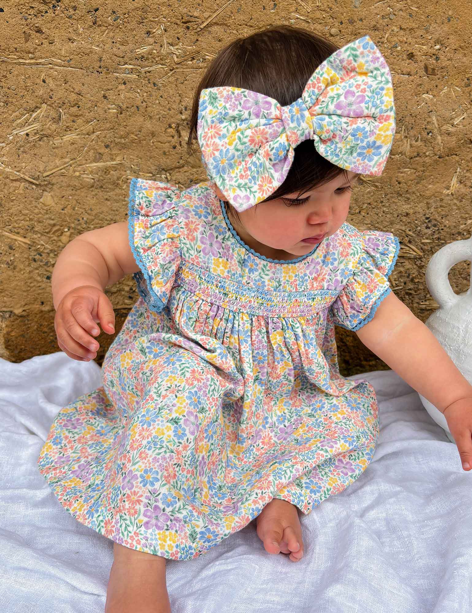 Baby in a floral dress and headband sitting on a textured surface