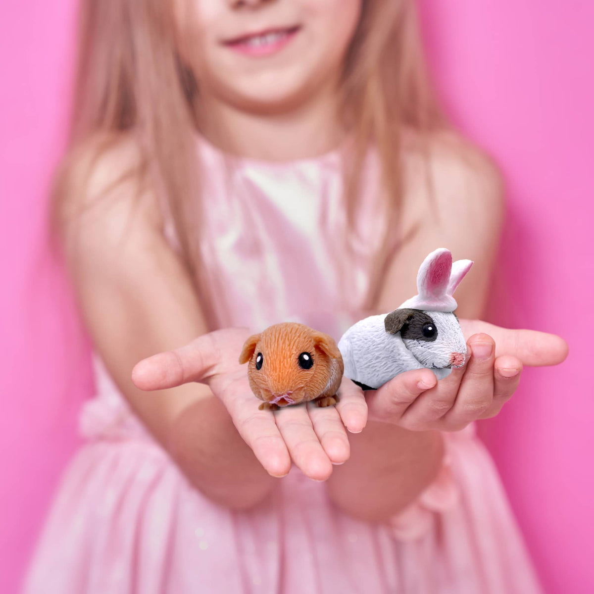 Child holding two small animal figurines against a pink background