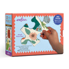 A child's hand interacting with the back of the open Eeboo Petite Pets 20-Piece Jigsaw Puzzle box, showing a cutout view of puzzle pieces inside alongside the product packaging.