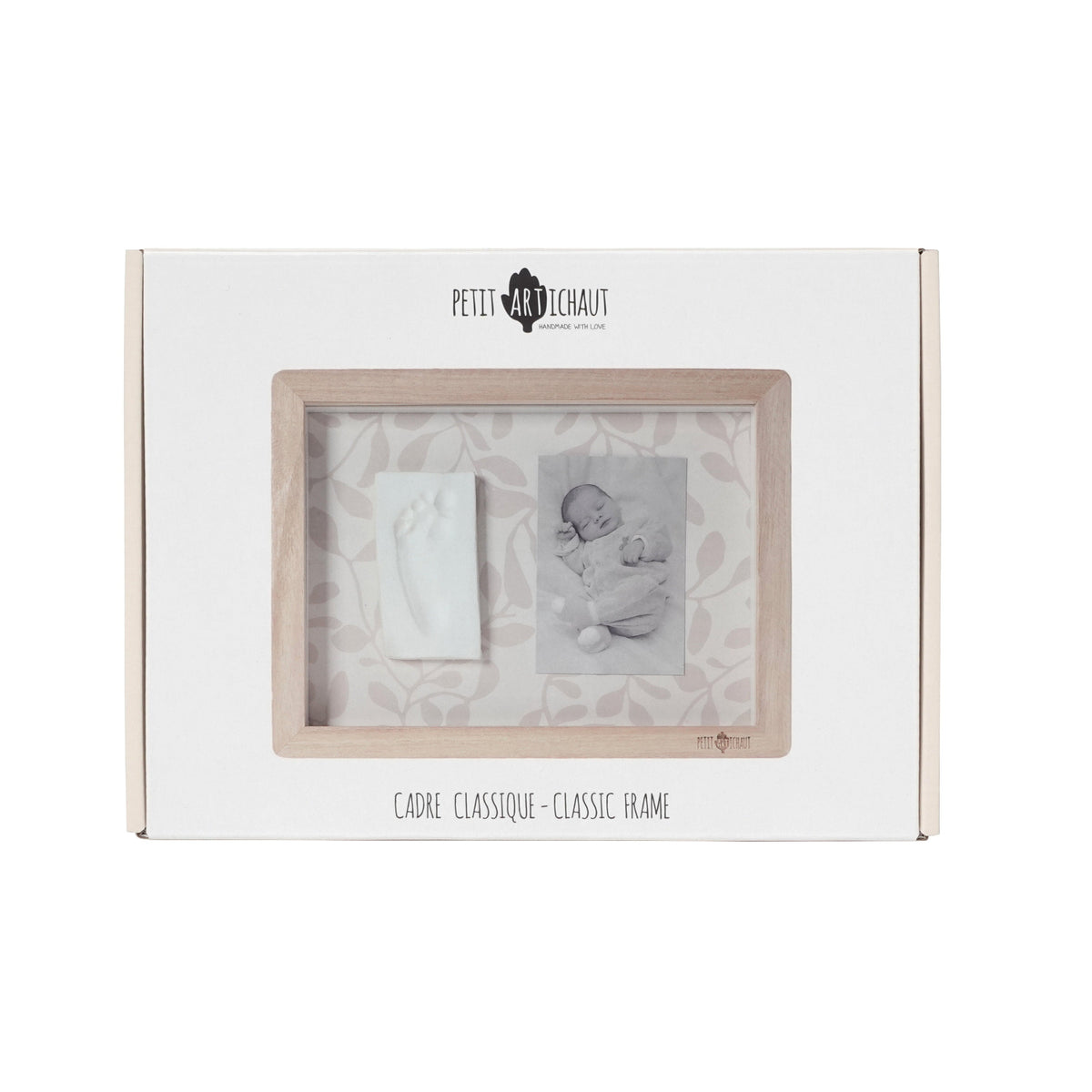 A white rectangular gift box for a baby keepsake photo frame set by Petit Maitre Chaut. The front of the box features a clear window displaying a light wood frame with two sample inserts: a white baby footprint print and a black-and-white newborn photo.