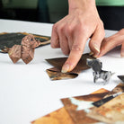 Person arranging leaf art of animals on a white surface