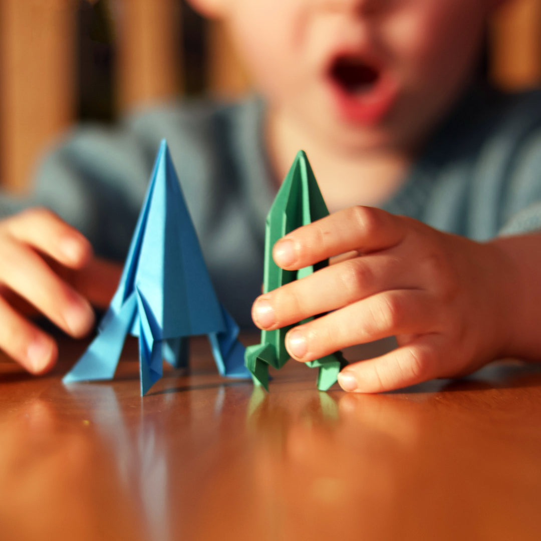 Child holding blue and green paper triangles on a wooden table