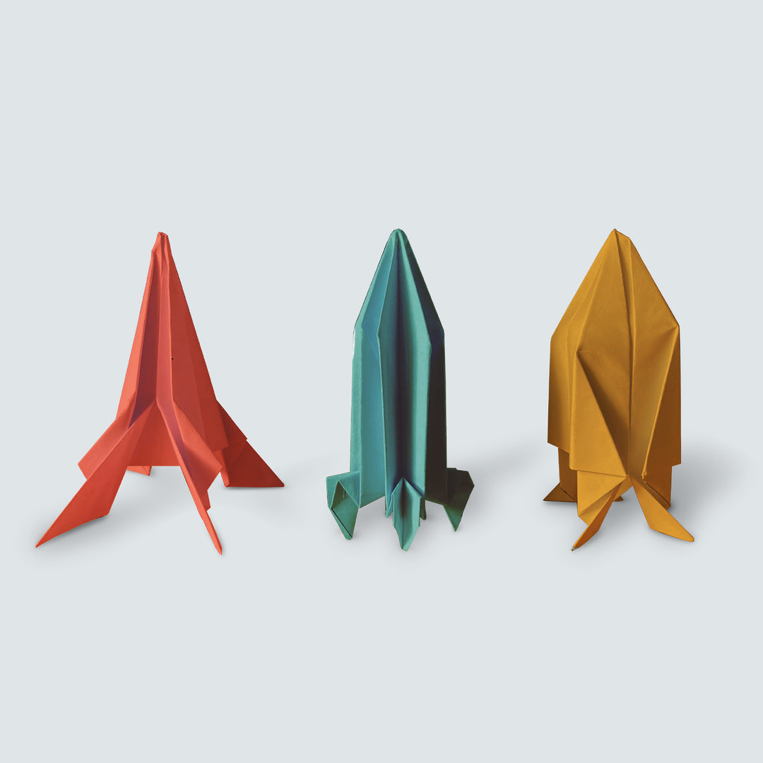 Three colorful paper rockets on a light gray background