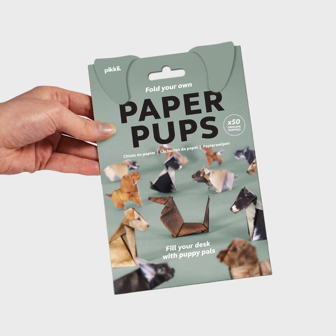 Packaging of paper puppets held by a hand on a light gray background