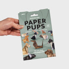 Packaging of paper puppets held by a hand on a light gray background