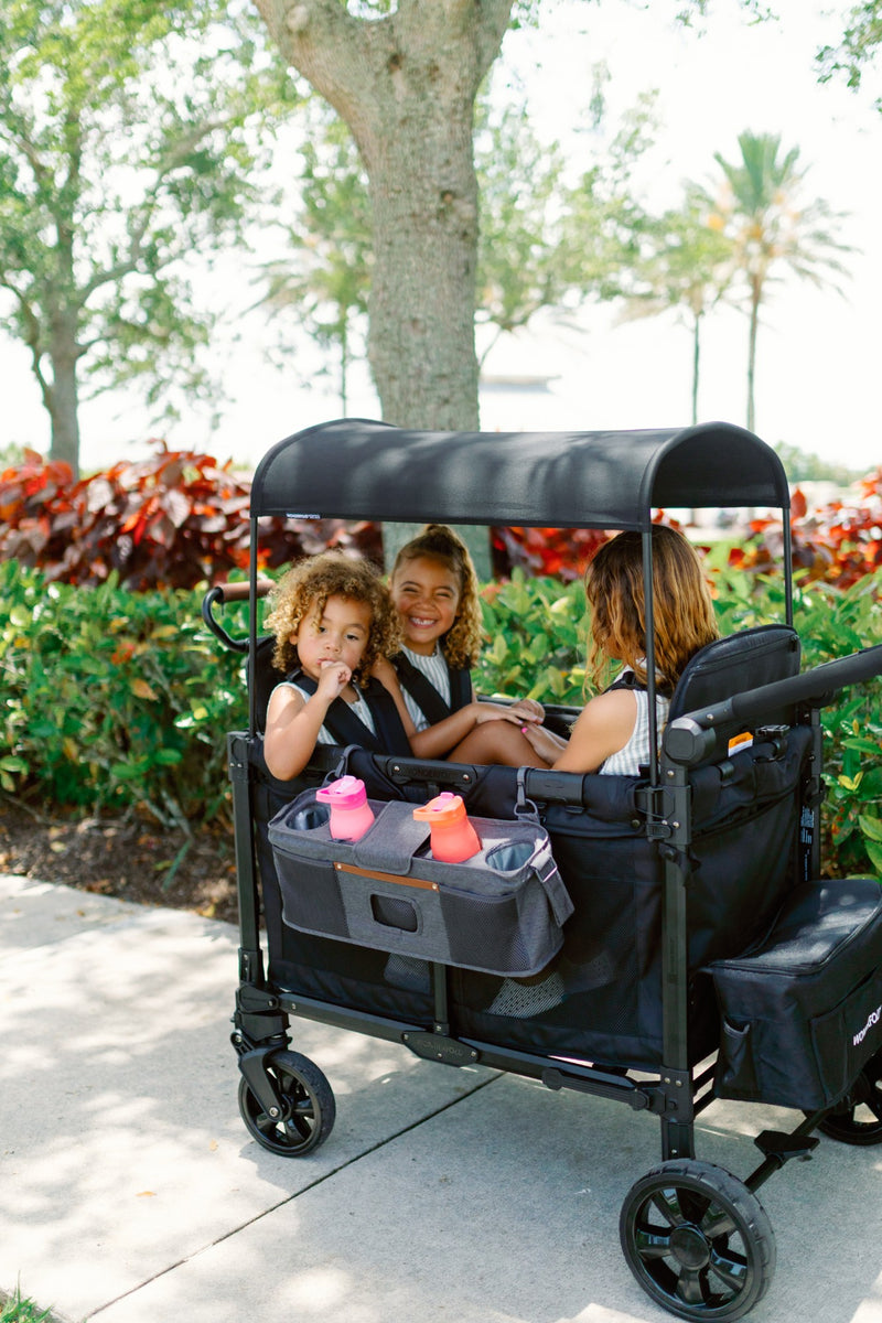 Black wagon with canopy in a park setting with children and a woman.