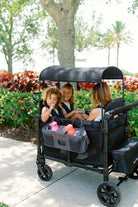 Black wagon with canopy in a park setting with children and a woman.