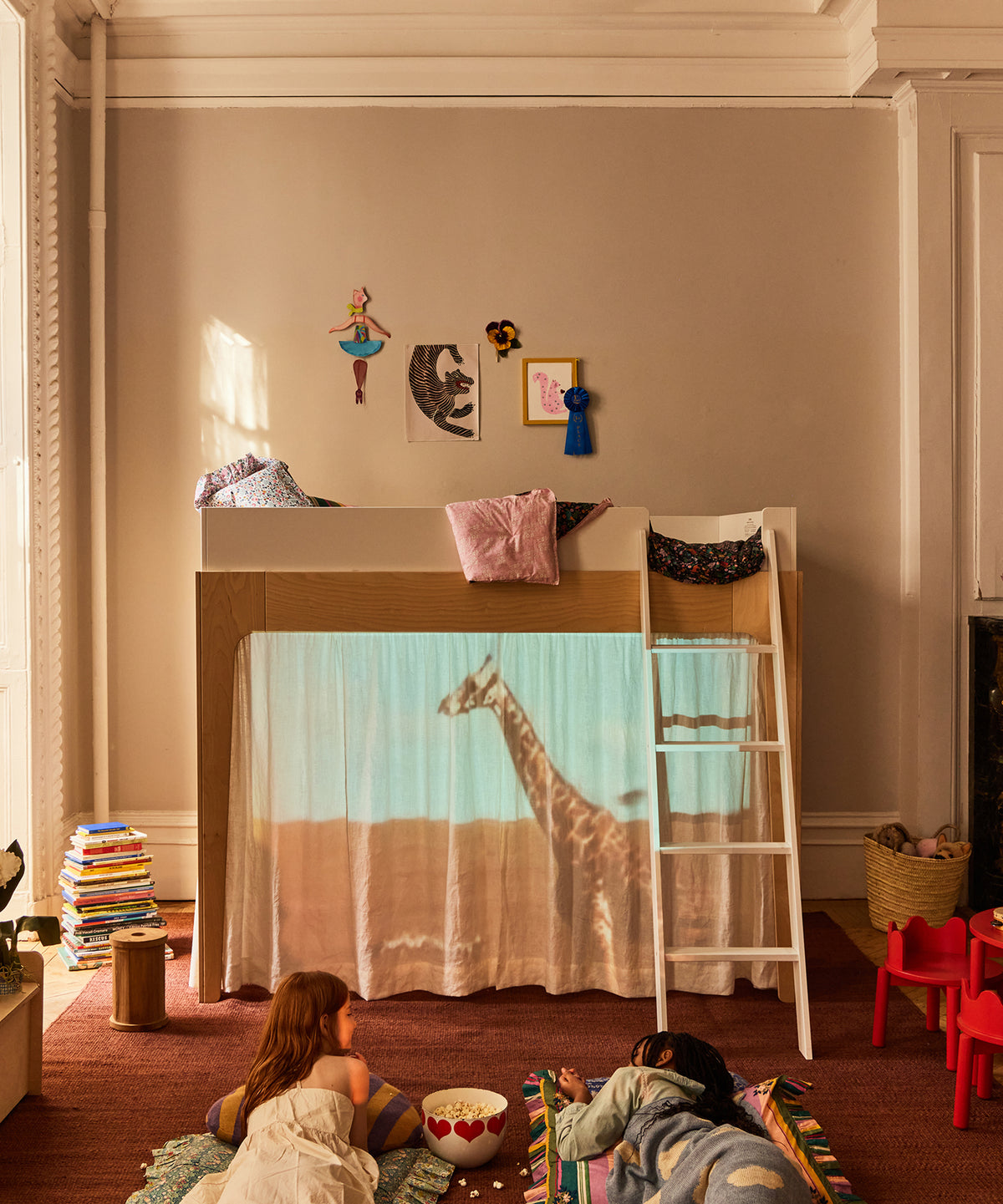 Children playing under a blanket fort with a giraffe投影在墙上，房间内有玩具和家具。