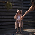 Child wearing a bear-themed robe holding hands with an adult against a wooden background