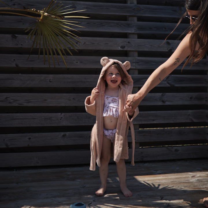 Child wearing a bear-themed robe holding hands with an adult against a wooden background