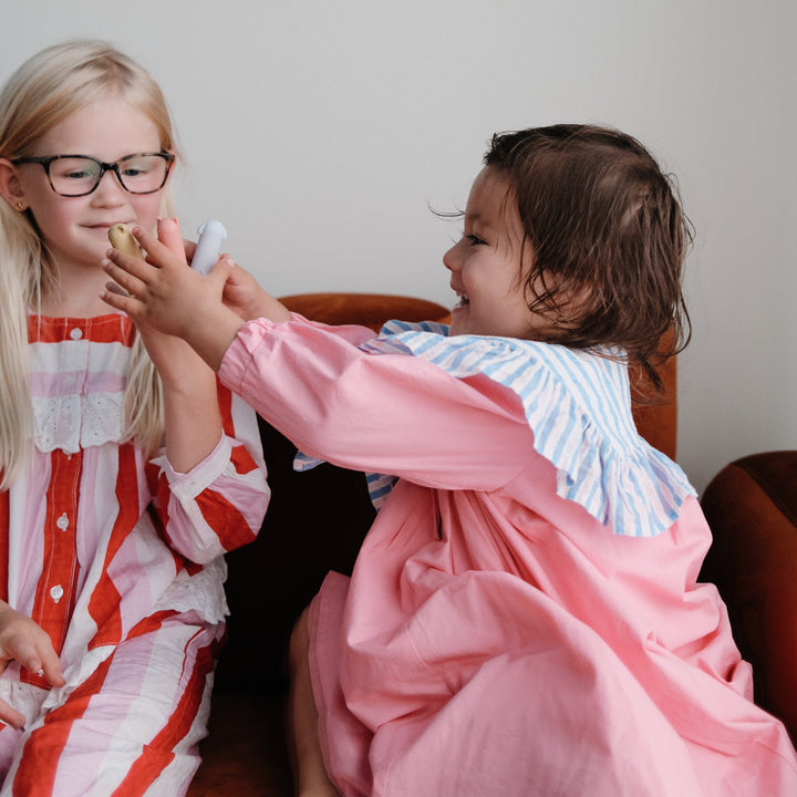 Two young girls sitting together, one in a red and white striped dress and the other in a pink outfit, sharing an object.