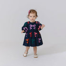 Child wearing a navy dress with colorful bow patterns on a white background