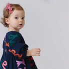 Child wearing a navy dress with colorful patterns against a plain background