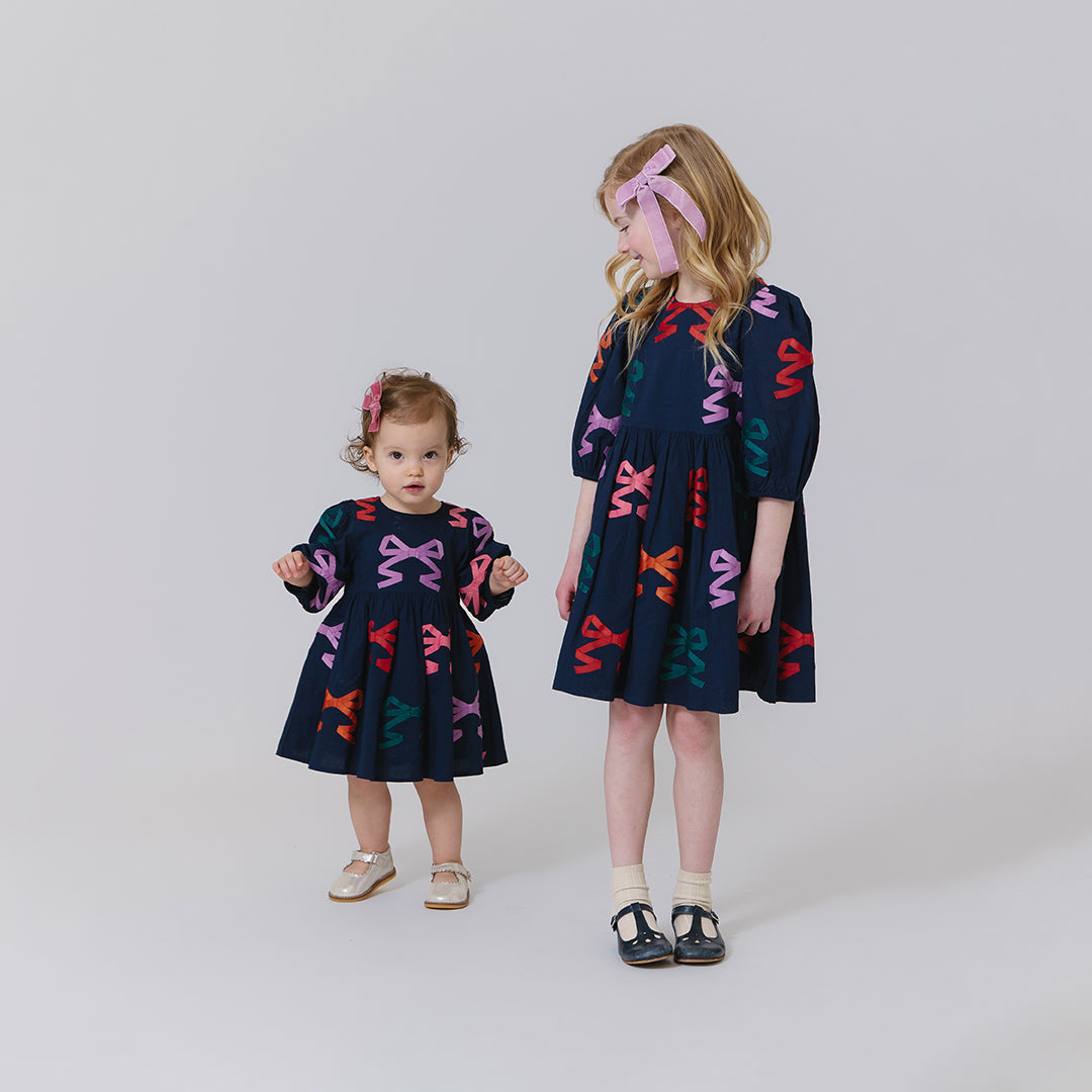 Two children wearing matching dresses with colorful patterns on a plain background