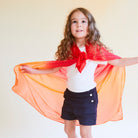 Child wearing a red and orange superhero cape against a plain background