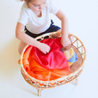 Child playing with a colorful fabric on a wicker stool against a white background