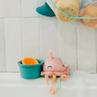 Pink knitted octopus toy with orange ball and blue bucket on a white surface.
