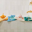 Colorful baby towels and plush toys on a bathroom counter with a tiled wall background.
