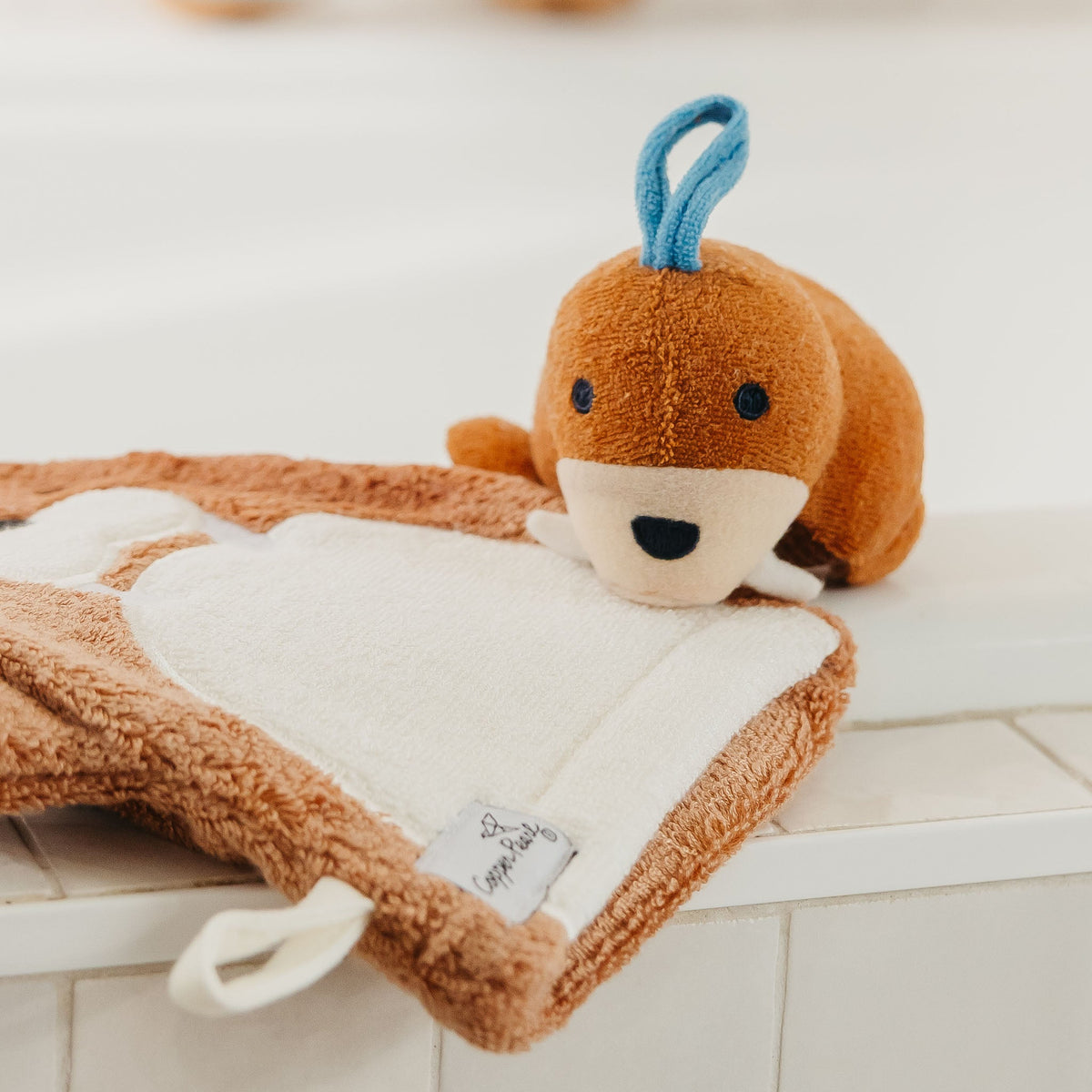 Brown plush toy with a blue tag on a white surface