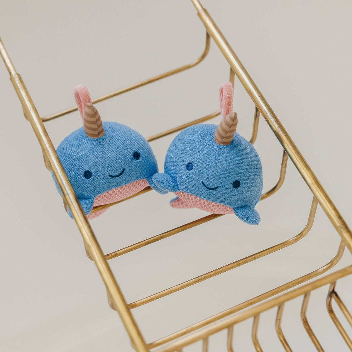 Two blue plush toys with pink and brown accents on a gold metal shelf.