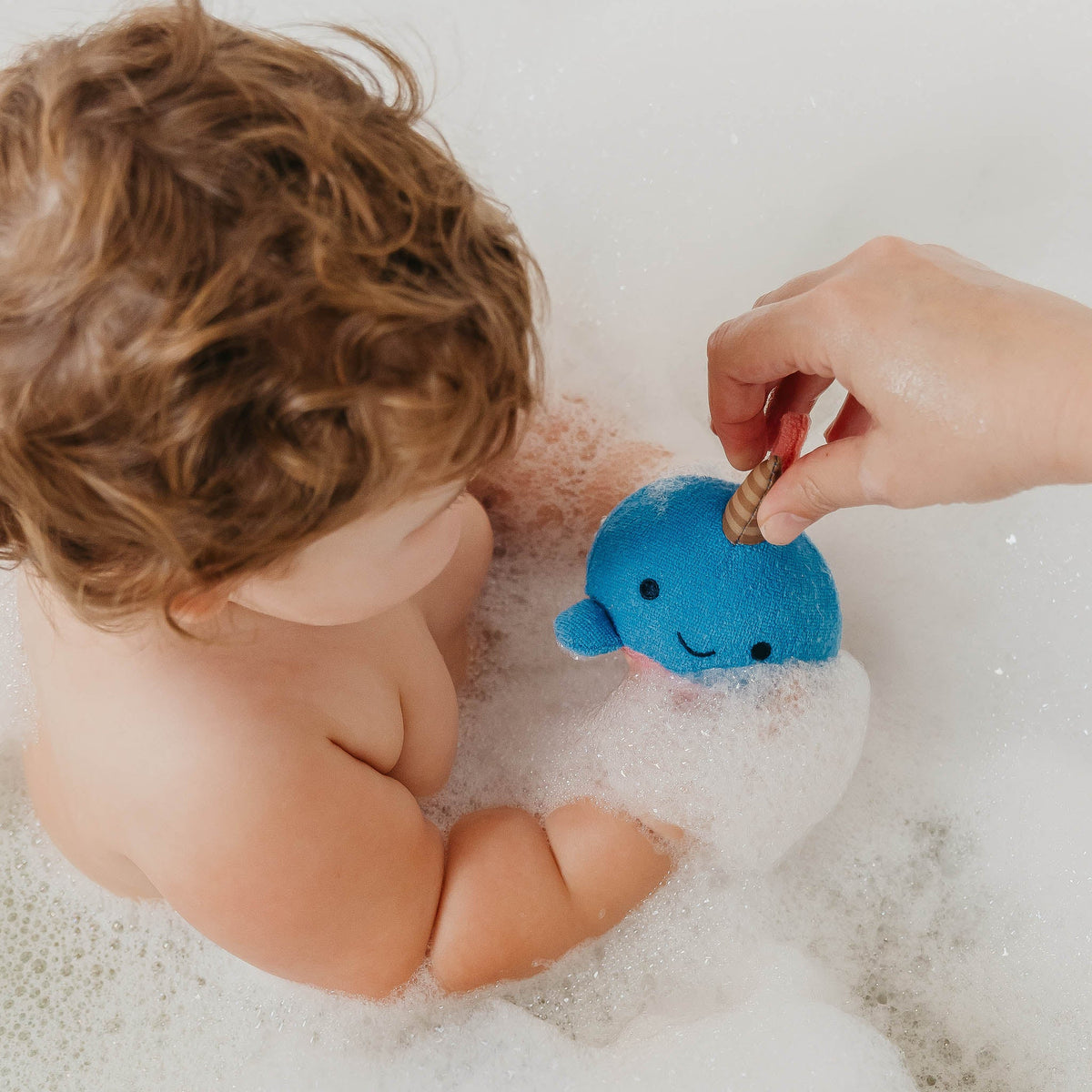 Child in a bubble bath with a blue plush toy