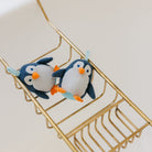 Two plush penguins on a gold wire shelf against a white background