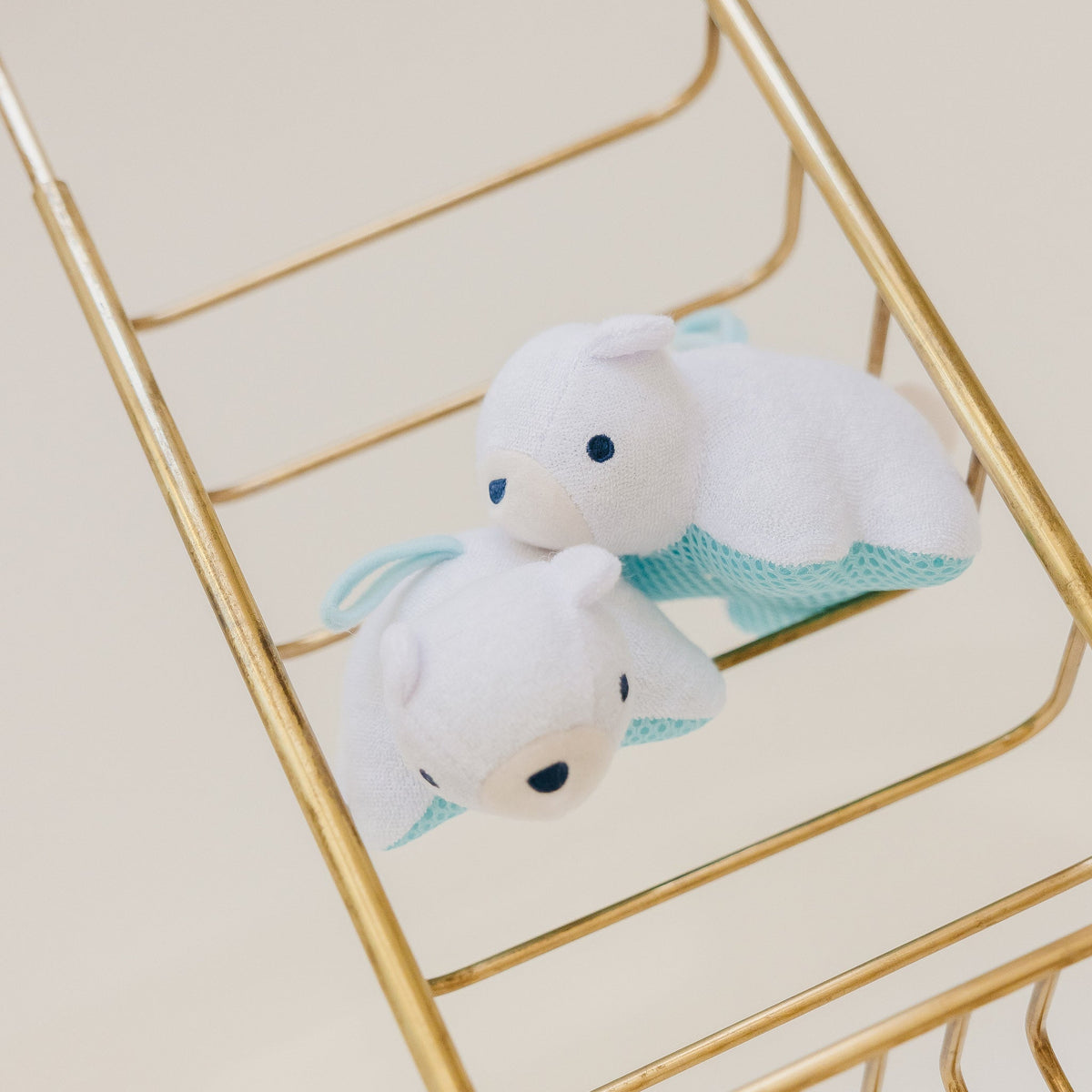 Two white plush toys with blue accents on a gold metal shelf.