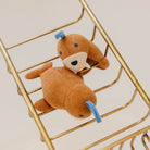 Small brown teddy bear with blue accents sitting inside a gold metal cart.