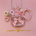 Collection of pink and gold hair accessories including a purse, headband, and clips on a pink background.