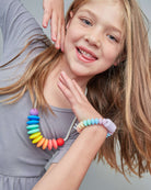 Young girl wearing a colorful beaded necklace and bracelet on a plain background