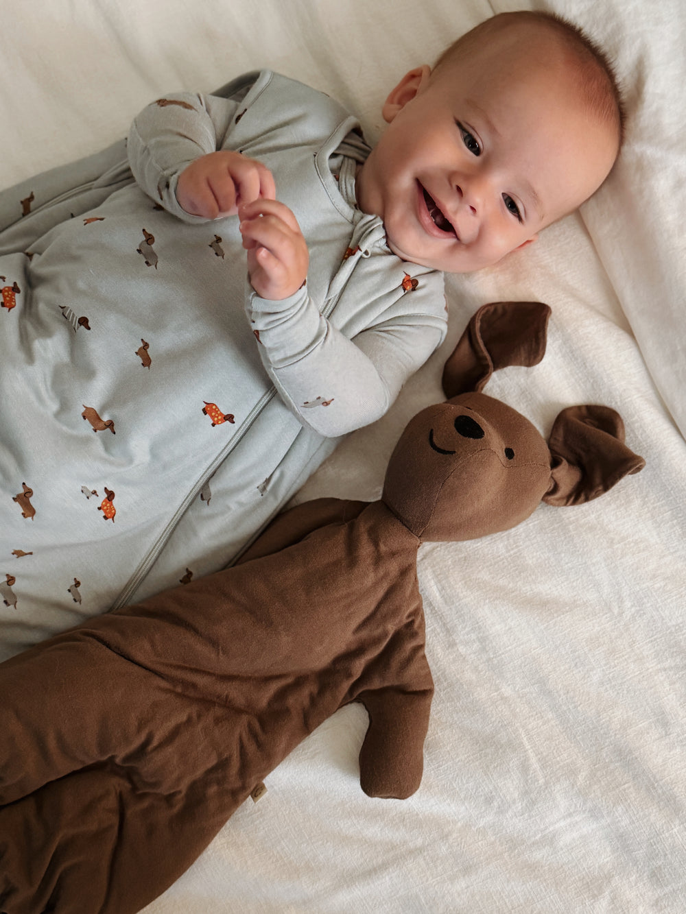 Baby lying on a white blanket with a brown plush toy