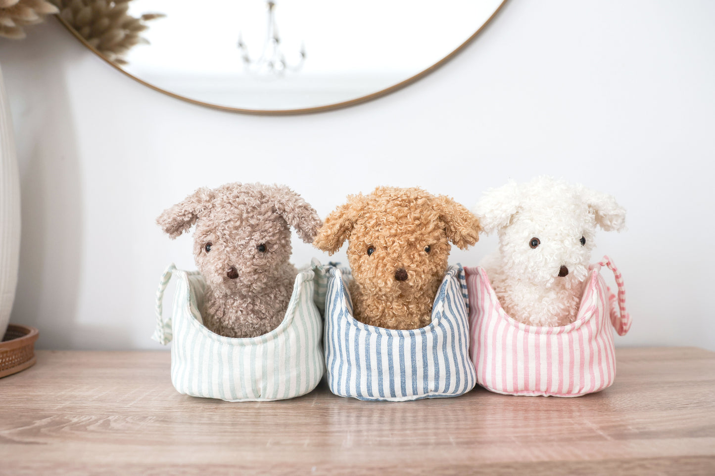 Three plush toys resembling dogs in colorful outfits on a wooden surface.