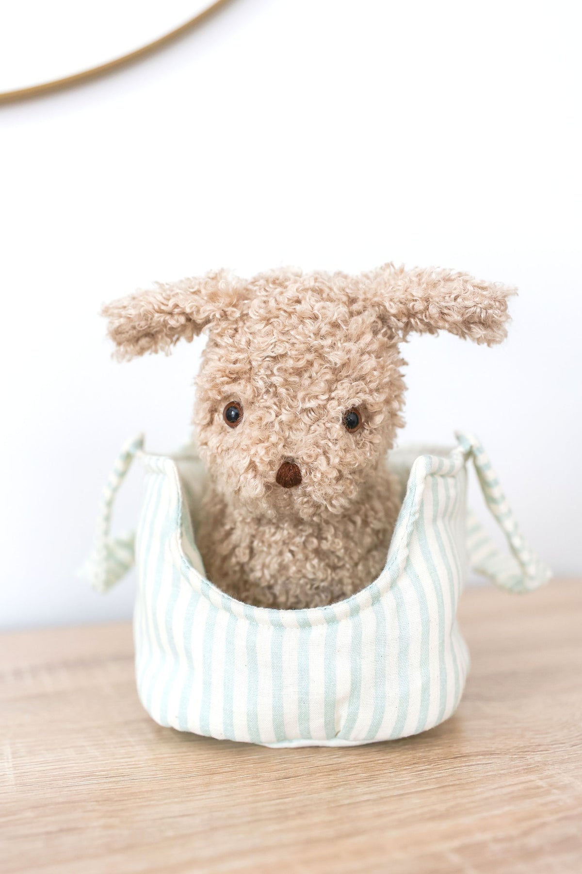 Small plush dog toy in a striped fabric basket on a wooden surface with a white background