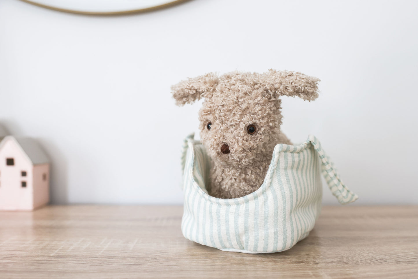 Stuffed animal toy in a striped bag on a wooden surface with a white wall background